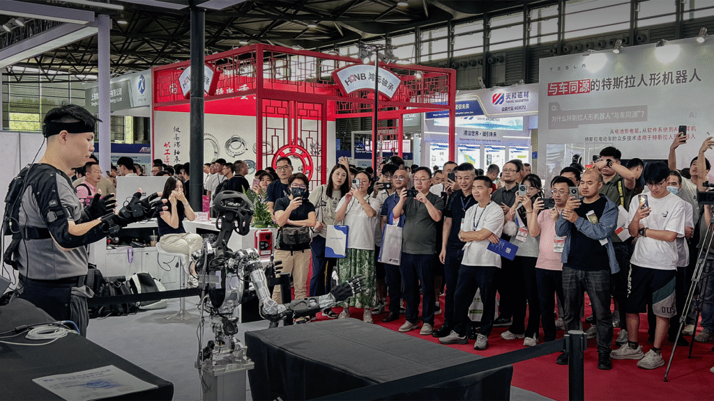 Photo of Adam-U humanoid robot demonstration at a robotics expo, with teleoperation suit and large audience, highlighting embodied AI data collection.