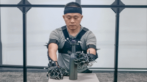 A Noitom Robotics operator performs a precision grasping task using a full-body motion capture system and instrumented gloves to record high-fidelity hand and arm movement data. The session supports humanoid teleoperation and embodied AI research by enabling robots to learn complex manipulation from human motion.