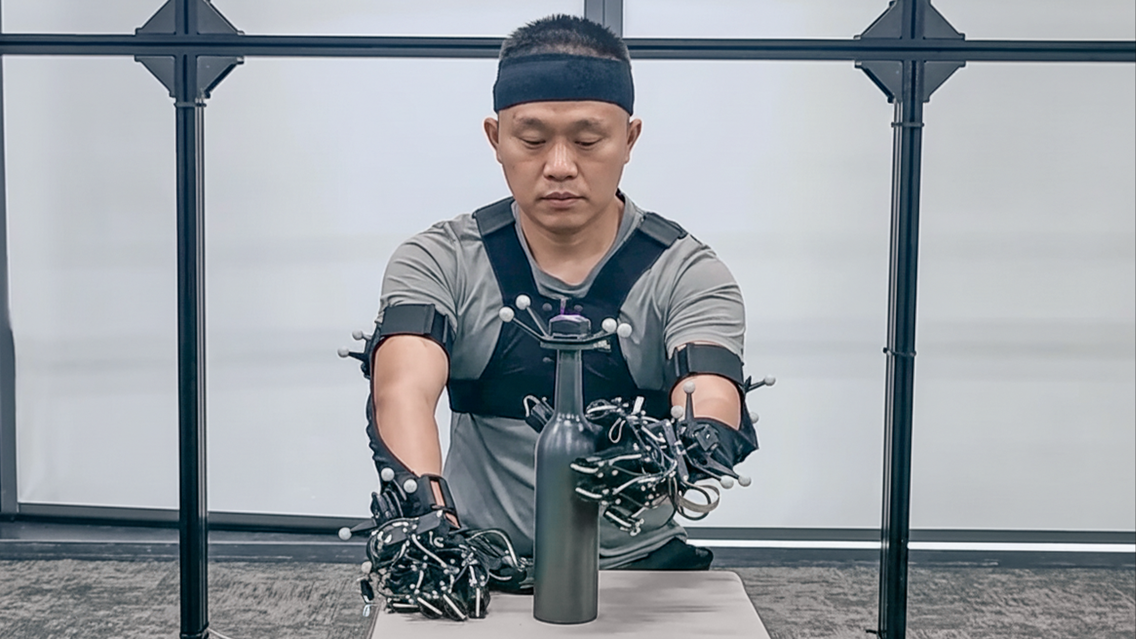 A Noitom Robotics operator performs a precision grasping task using a full-body motion capture system and instrumented gloves to record high-fidelity hand and arm movement data. The session supports humanoid teleoperation and embodied AI research by enabling robots to learn complex manipulation from human motion.